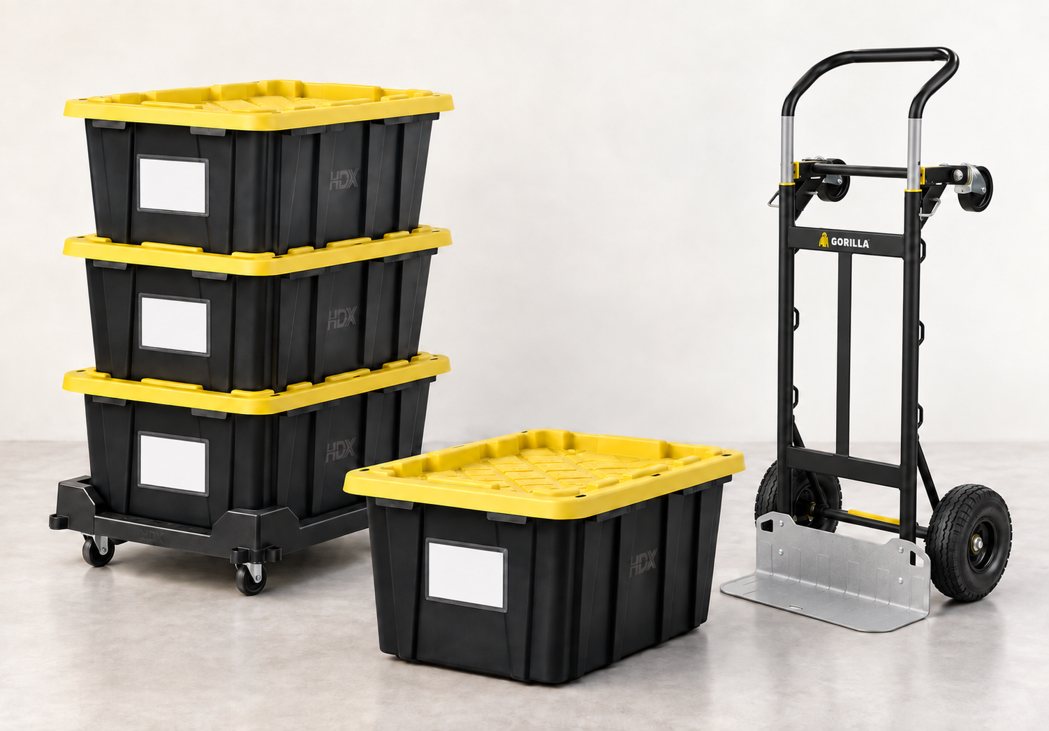 Three stacked black 27-gallon HDX totes with yellow lids and room cards on a rolling tote dolly, a fourth tote beside them, and a Gorilla convertible hand truck.